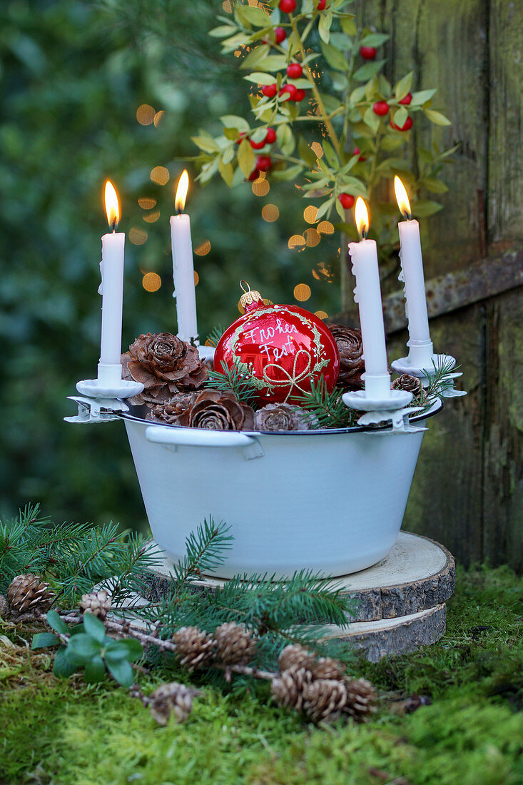 Advent arrangement with candle clips on edge of enamel bowl on moss outside