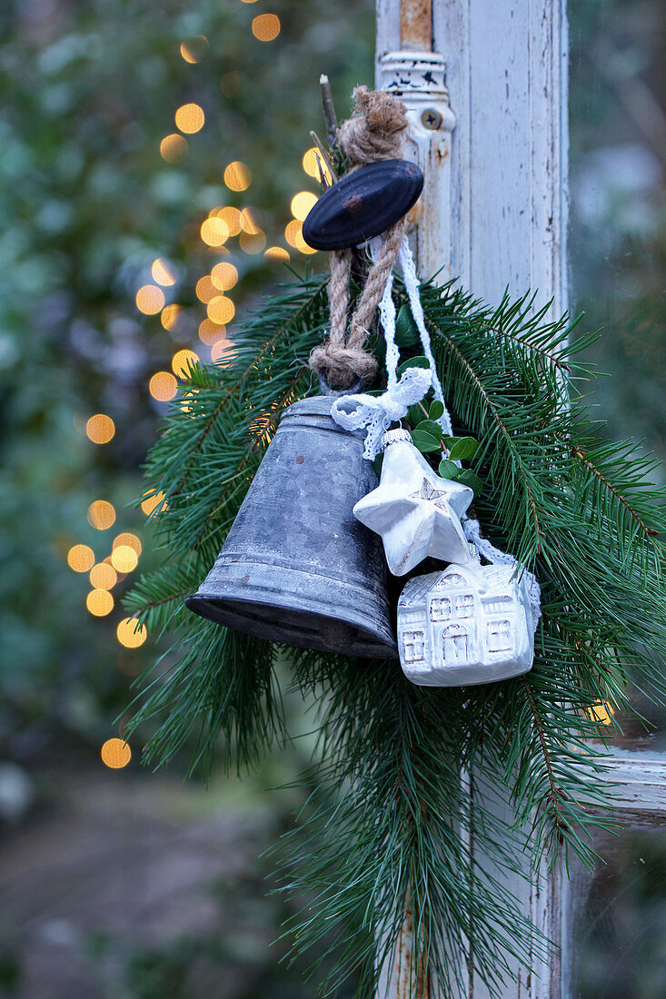 Arrangement of fir branches, bell, star and small house hung from window handle
