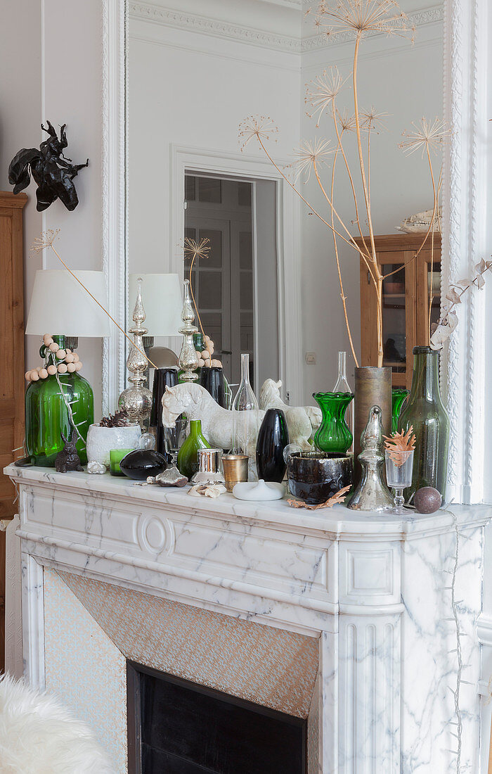 Dekoobjekte und Lampe mit grünem Glasfuß auf Kaminsims mit Spiegel