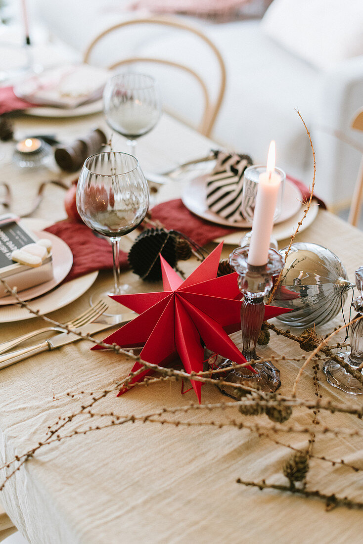 Weihnachtstisch mit rotem Papierstern, Lärchenzweigen und Kerze