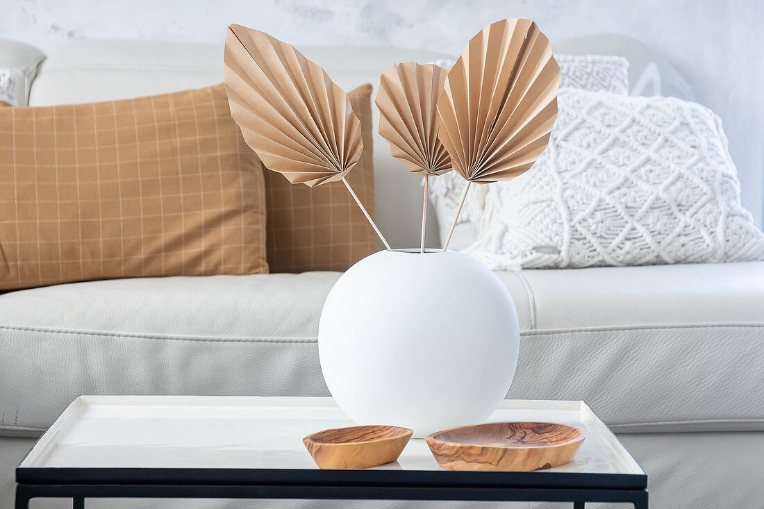 DIY palm leaves made from brown paper in white spherical vase on coffee table