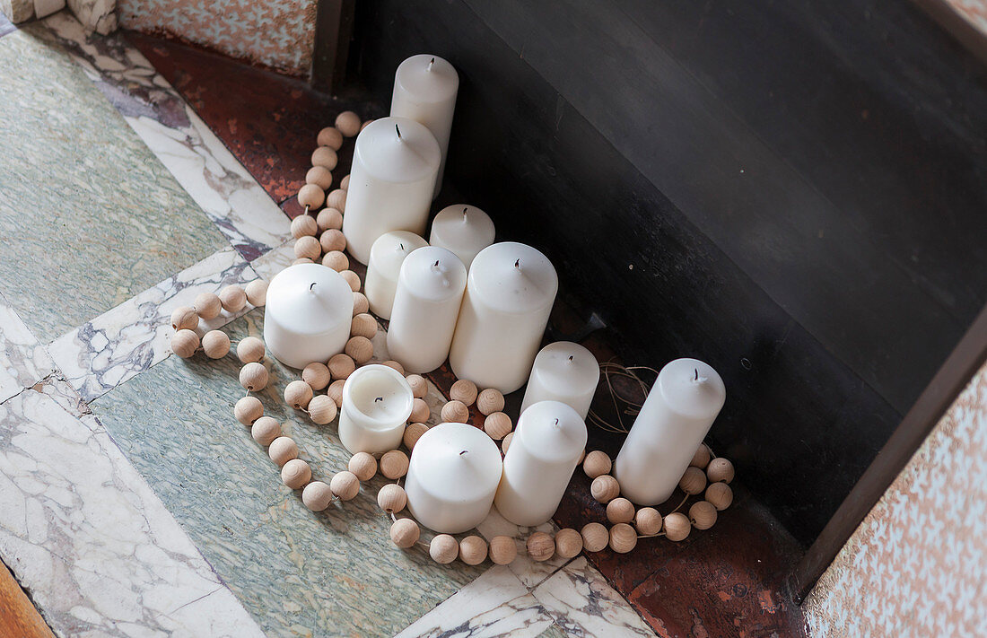 White pillar candles and wooden beads in front of fireplace