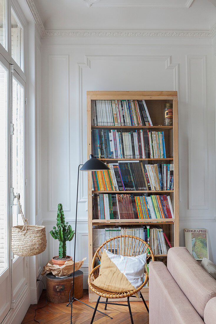 Bücherschrank, Rattanstuhl und Stehlampe vor Fenster im Wohnzimer