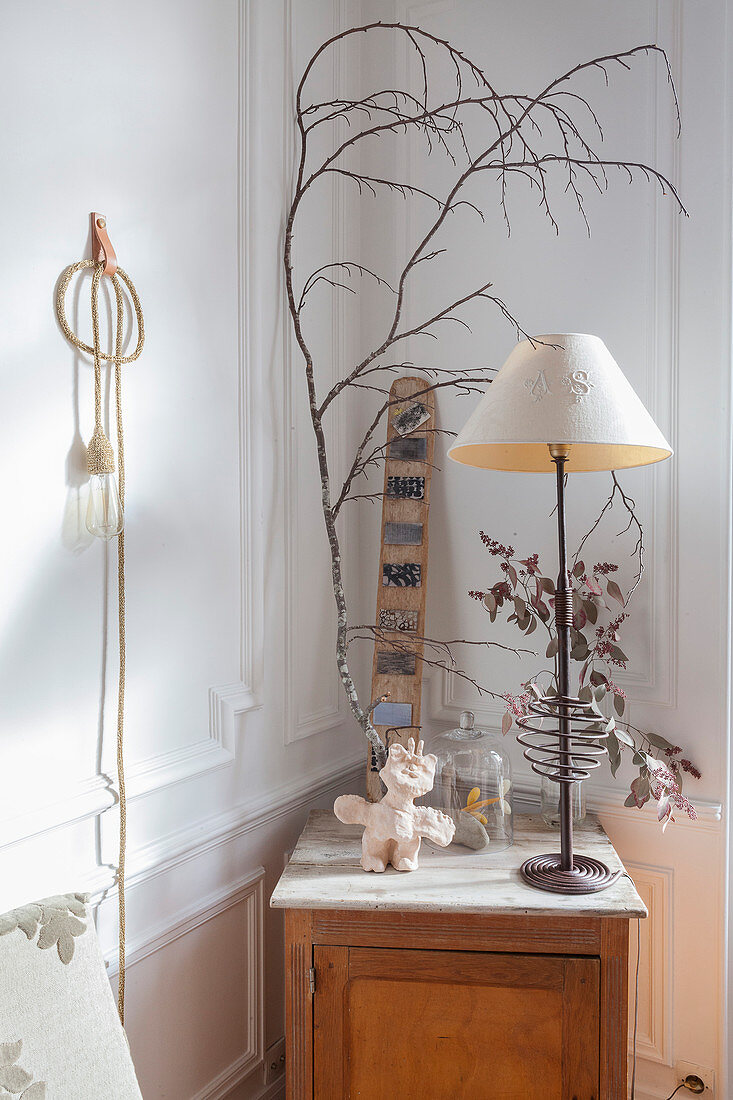 Holzschränkchen mit Lampe, Ast und Trockenblume in Zimmerecke