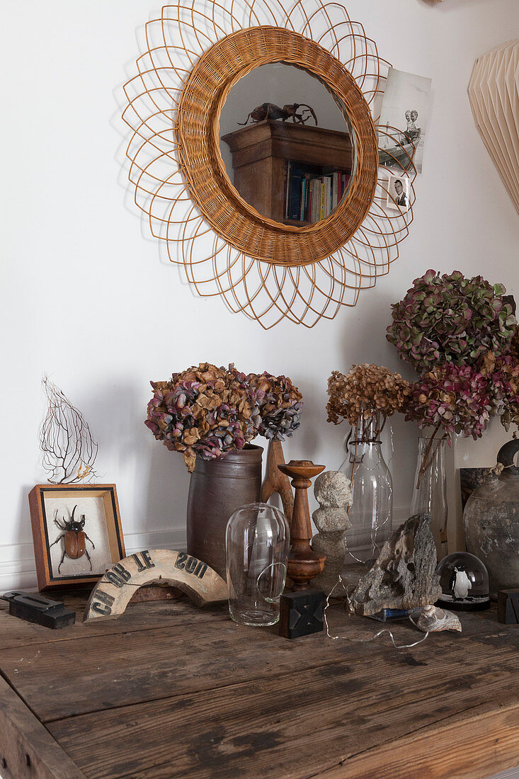 Vasen mit Trockenblumen auf altem Holztisch, darüber Wandspiegel