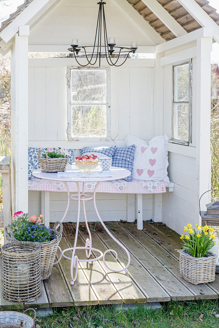 Romantische Kissen auf der Bank in der Gartenlaube mit kleiner Terrasse