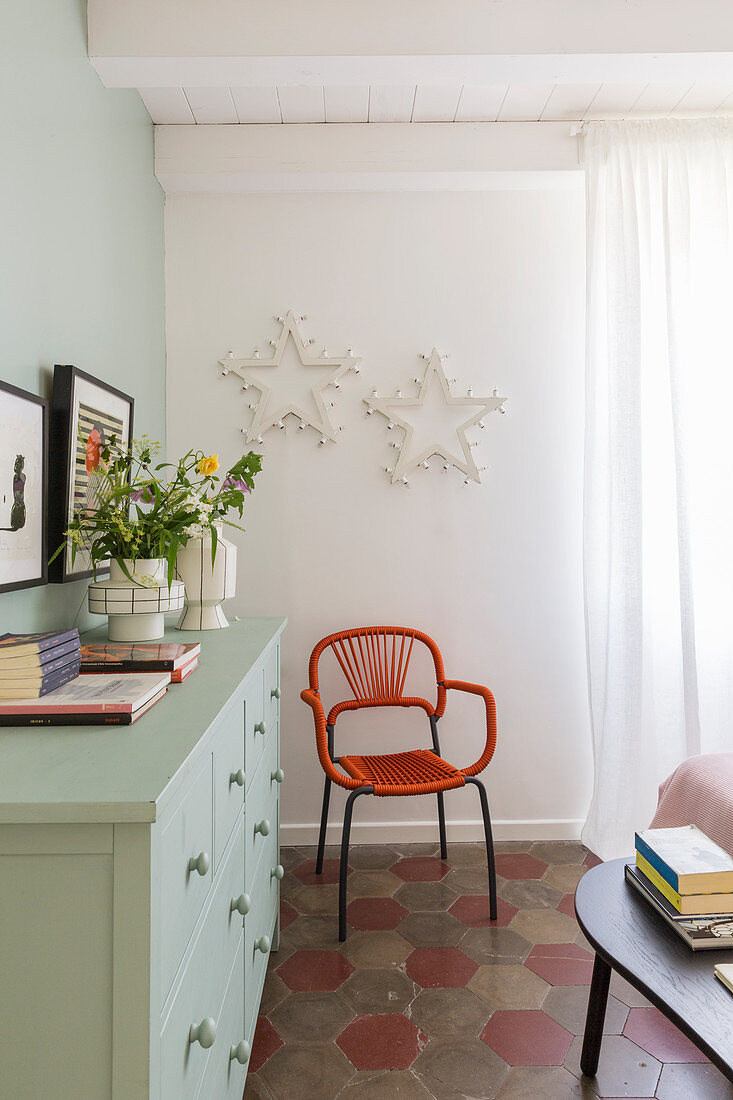 Orange chair below star-shaped lamps on wall and next to sideboard