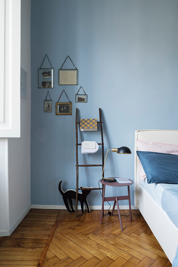 Leiter als Ablage und Nachttisch vor blauer Wand im Schlafzimmer