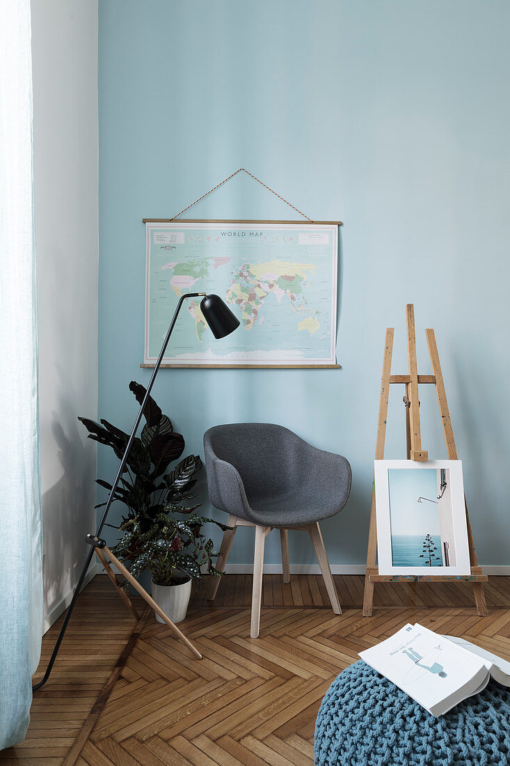 Armchair, plants and easel below map of the world on pale blue wall