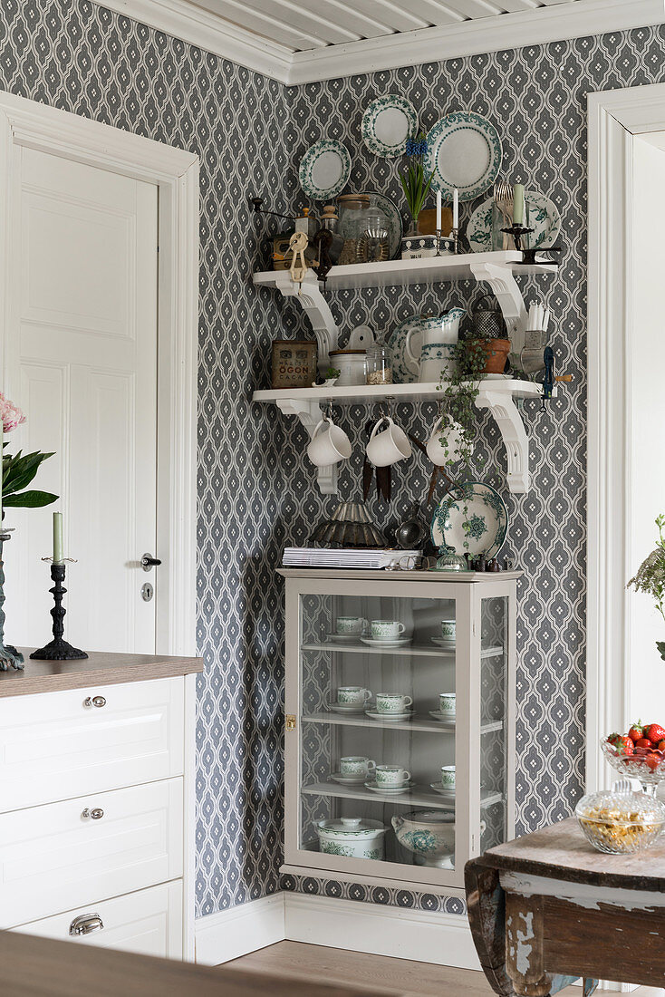 Shelves and display case mounted on wall with patterned wallpaper in country-house kitchen