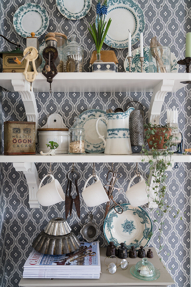 Crockery on shelves on wall with patterned wallpaper in country-house kitchen