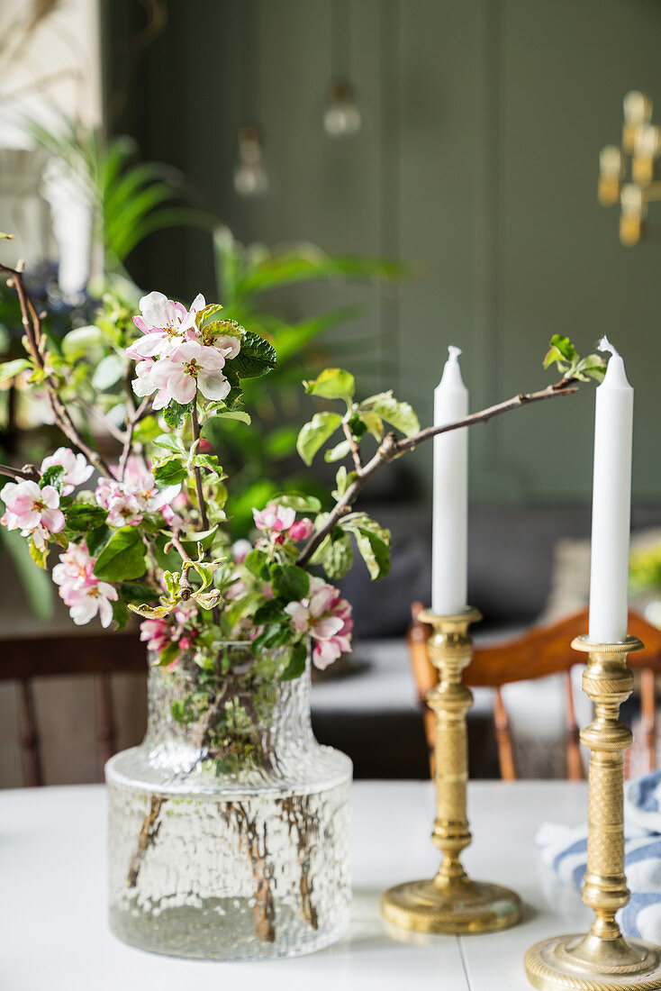 Glasvase mit Blütenzweig und Kerzen auf Esstisch