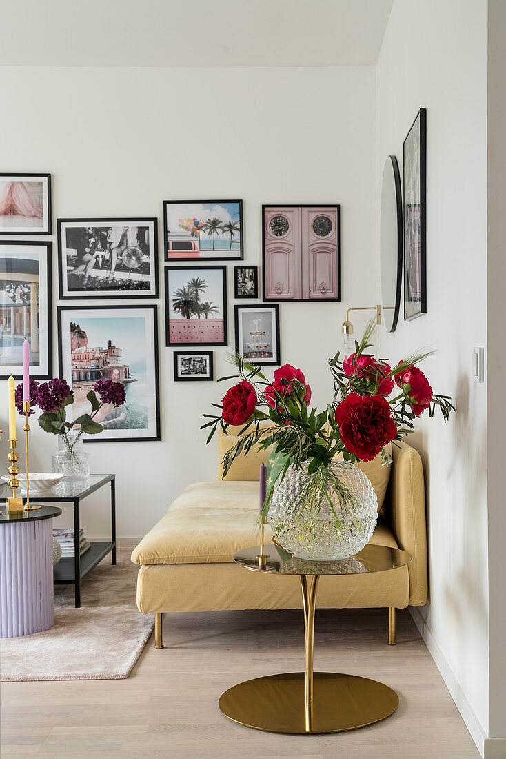 Glass vase of red peonies, sofa and gallery of photographs on wall of living room