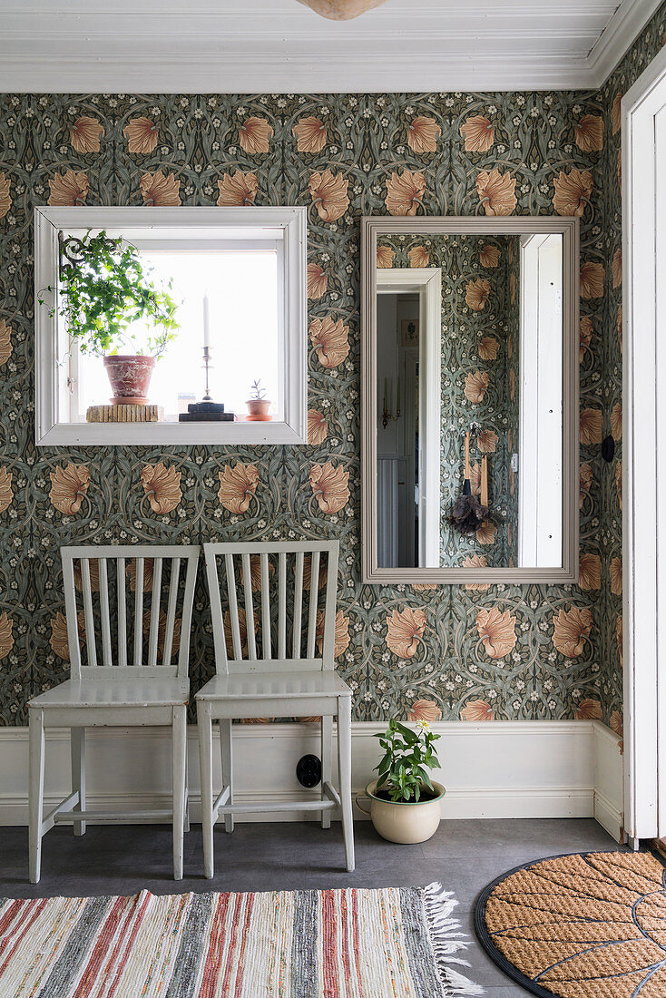Two chairs below mirrors on wall with William Morris floral wallpaper in hallway