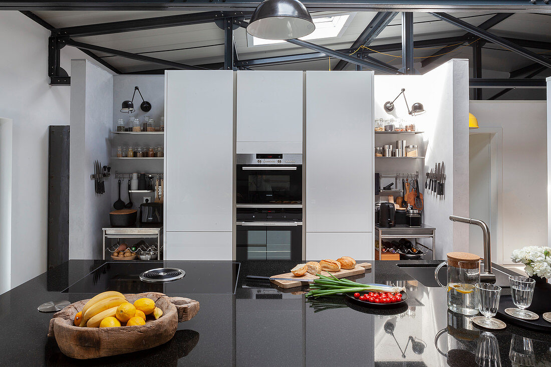 Island counter with black, high-gloss worksurface in open-plan kitchen
