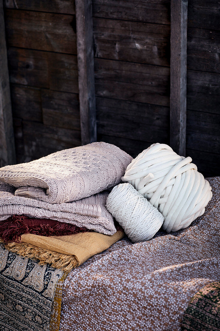 Pile of folded blankets, spool of yarn and ball of wool in front of board wall