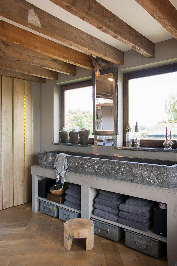 Stone trough used as sink in rustic bathroom with wood-beamed ceiling