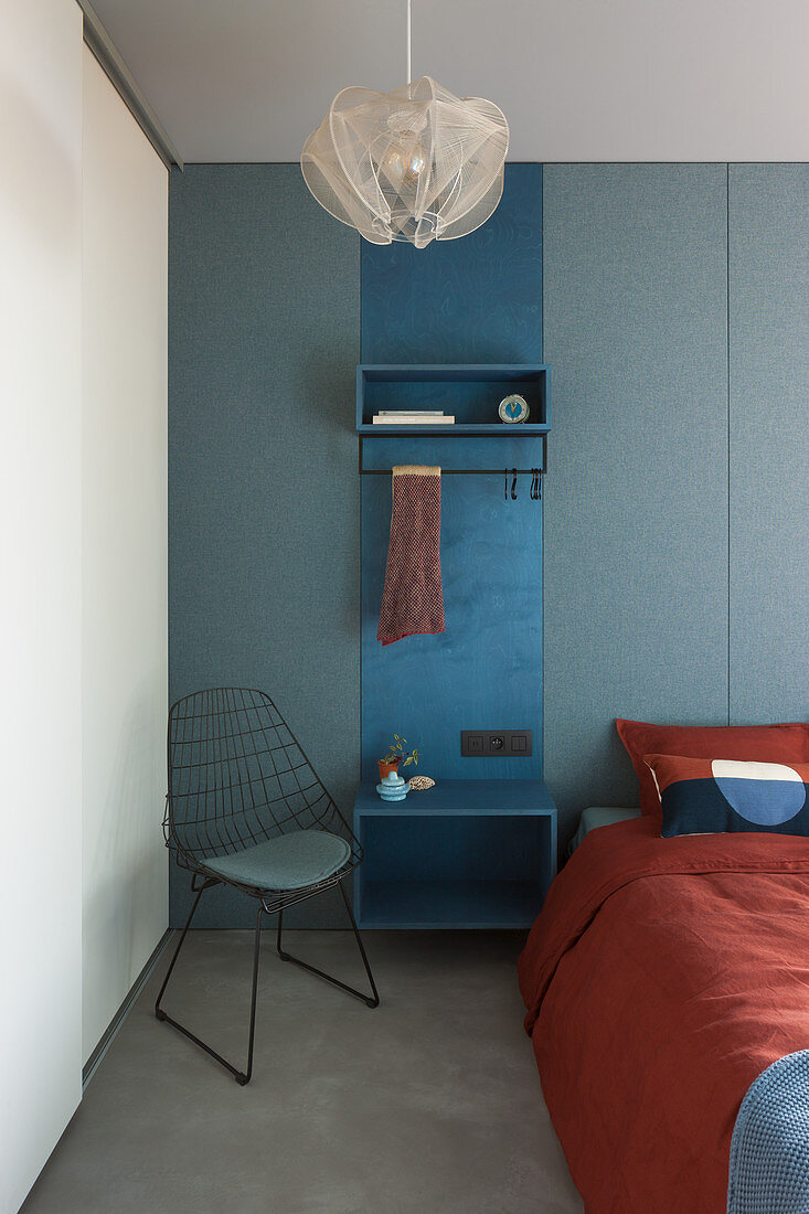 Blue cloakroom panel used as bedside table between bed and wire chair