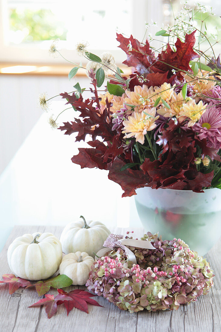 Strauß aus Chrysanthemen mit Herbstlaub, weiße Kürbisse mit Kranz aus Hortensienblüten und rosa Pfeffer, Blätter vom Amberbaum