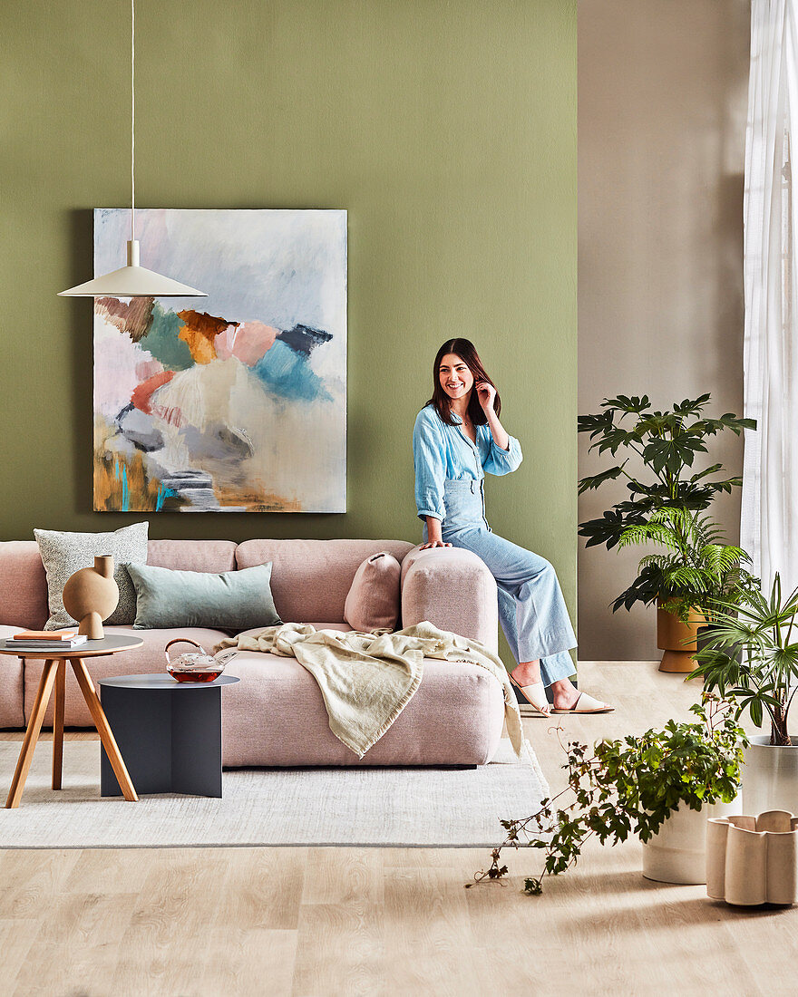 Pastel pink upholstered sofa in front of green wall with picture, brunette woman at the sofa