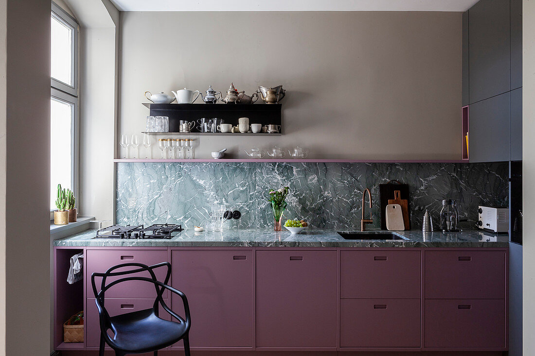Black chair next to kitchen counter with berry-coloured cabinets