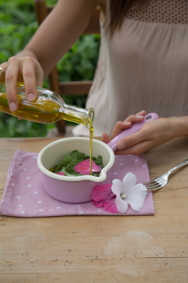 Preparing a mallow poultice: cover mallow leaves and flowers with olive oil