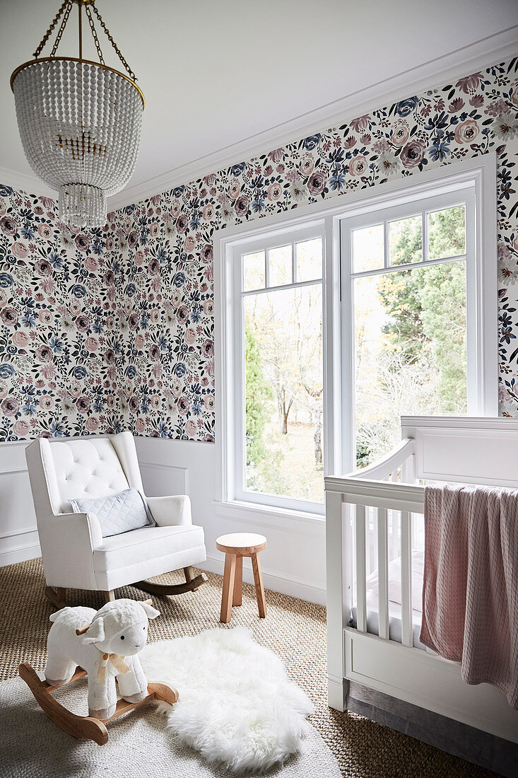 Baby cot, upholstered rocking chair and rocking sheep in the children's room with wallpaper