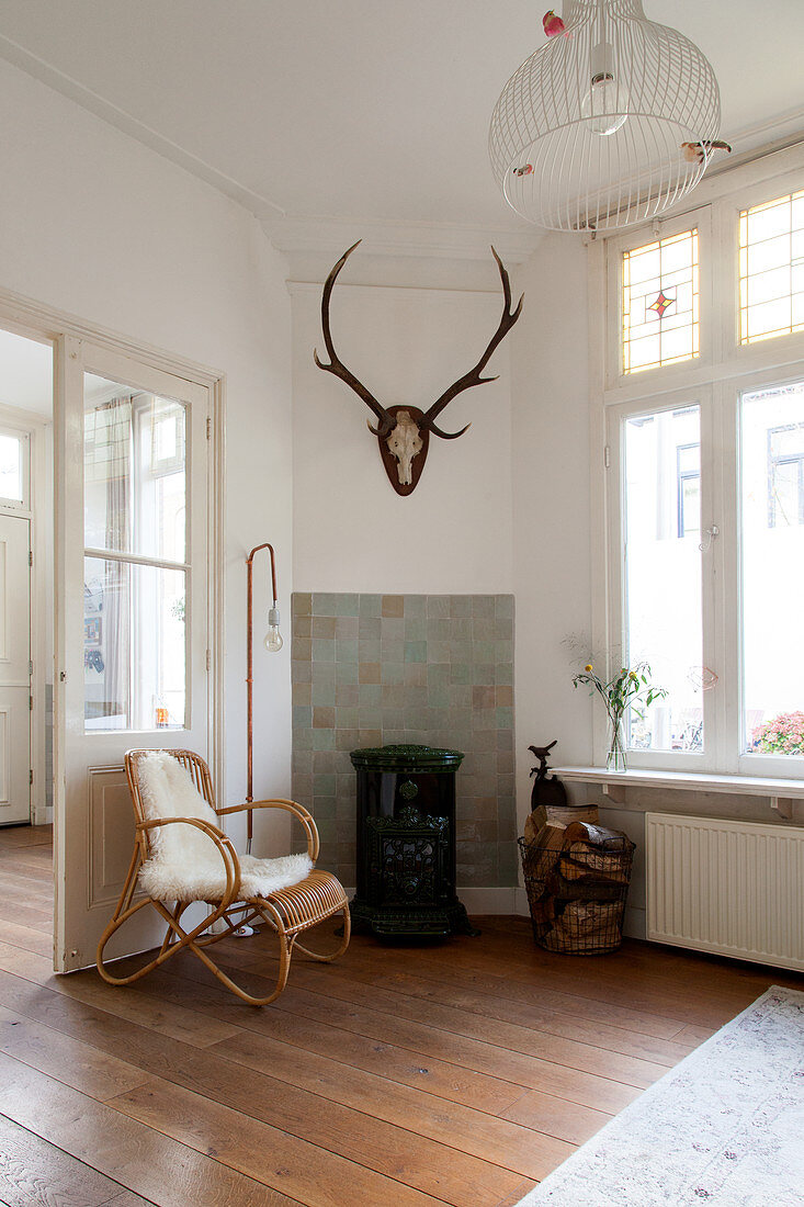 Rattan armchair, standard lamp, hunting trophy and log burner in corner