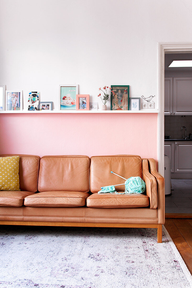 Leather sofa against pink wall below photos and pictures on ledge