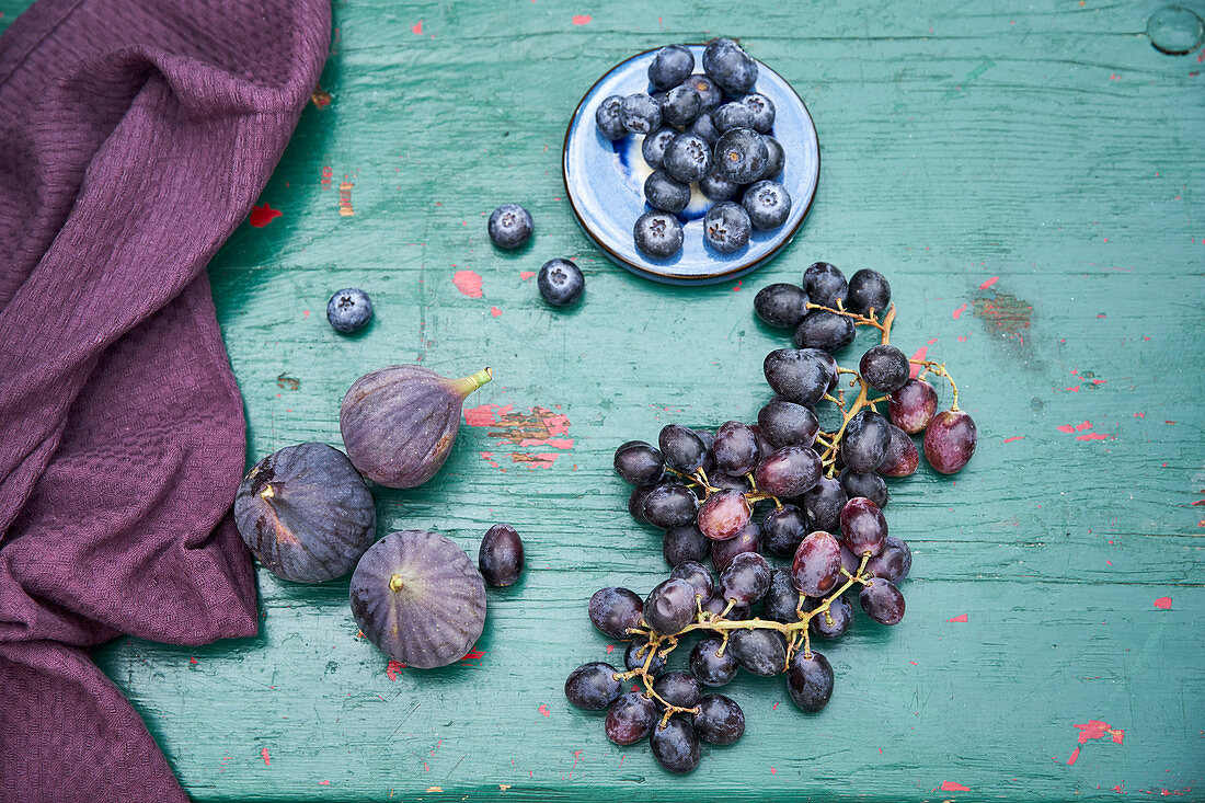 Blaubeeren, Trauben und Feigen auf türkisfarbenem Holztisch