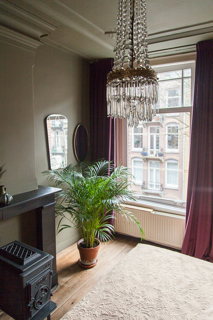 Chandelier above double bed, cast iron stove and potted palm in bedroom