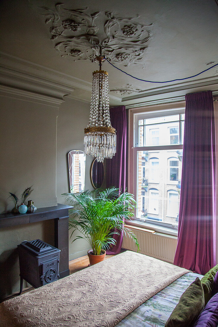 Chandelier above double bed, cast iron stove and potted palm in bedroom