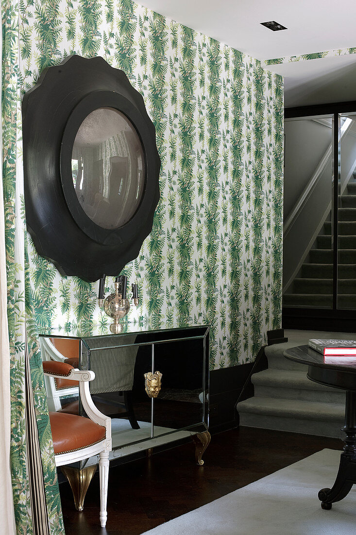 Mirrored sideboard below convex mirror on wall with botanical wallpaper