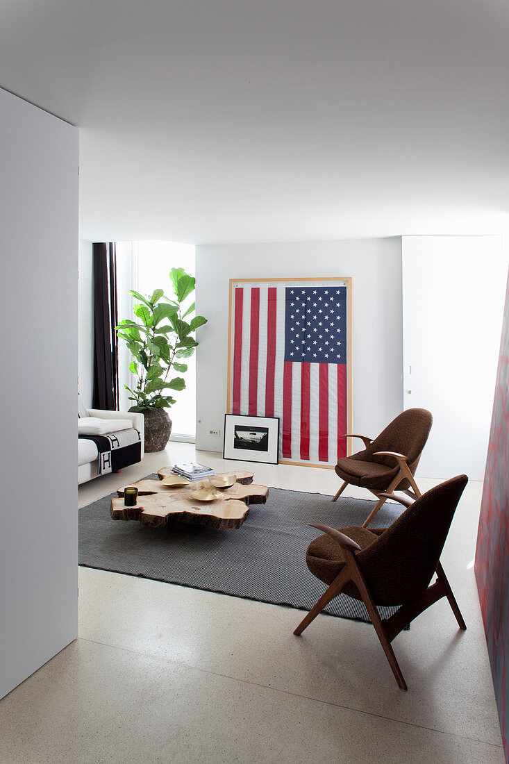 Chairs around coffee table made from slice of tree trunk in front of a Stars and Stripes flag on wall