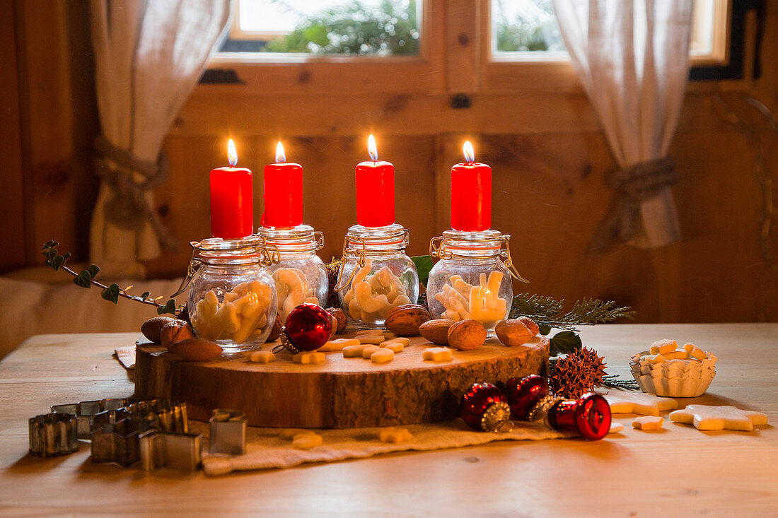 Vier rote Kerzen auf Einmachgläsern mit Plätzchen als Adventskranz