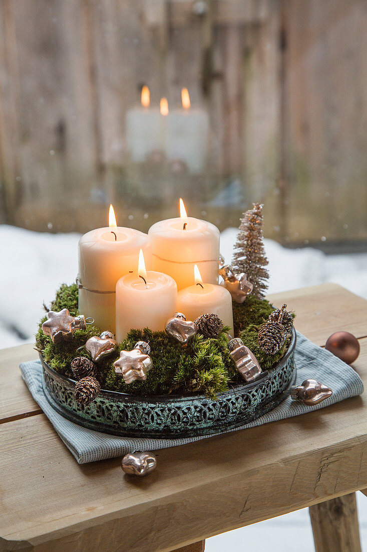 Four white pillar candles, moss and decorations on metal tray