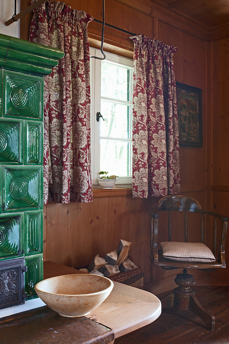 Alter Drehstuhl am Fenster neben klassischem Kachelofen in der Stube