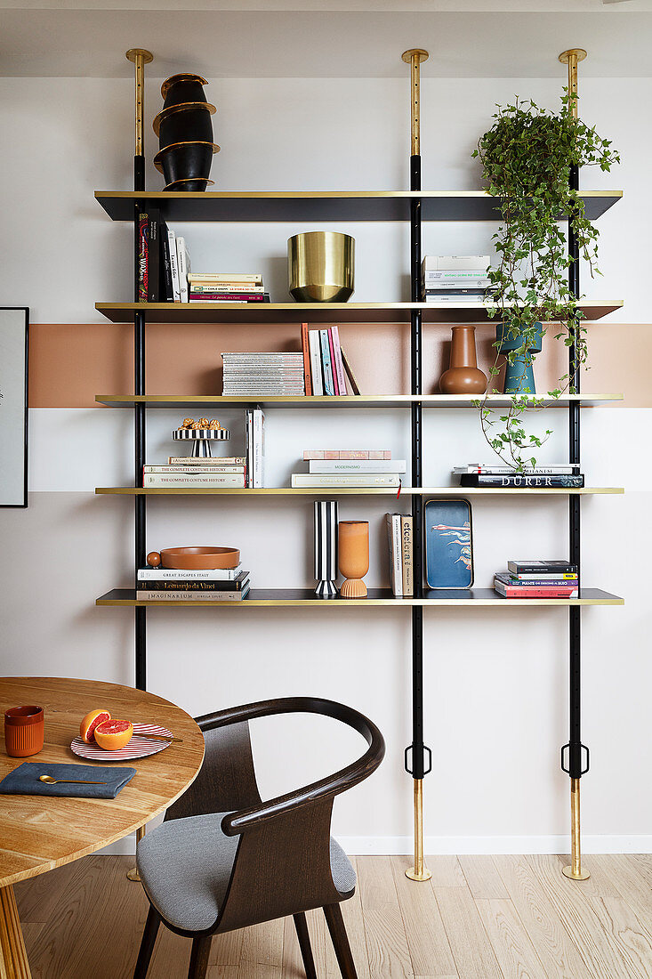 Offenes Bücherregal, davor runder Holztisch mit Designerstuhl