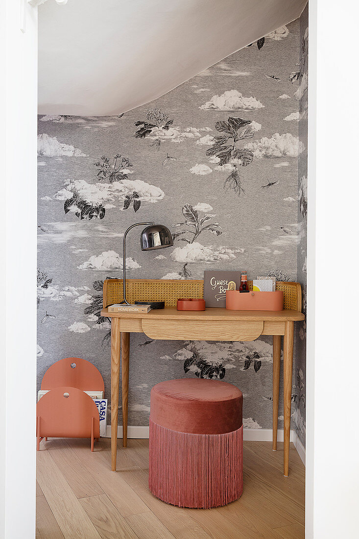 A desk and a pouf in a guest room with monochrome wallpaper