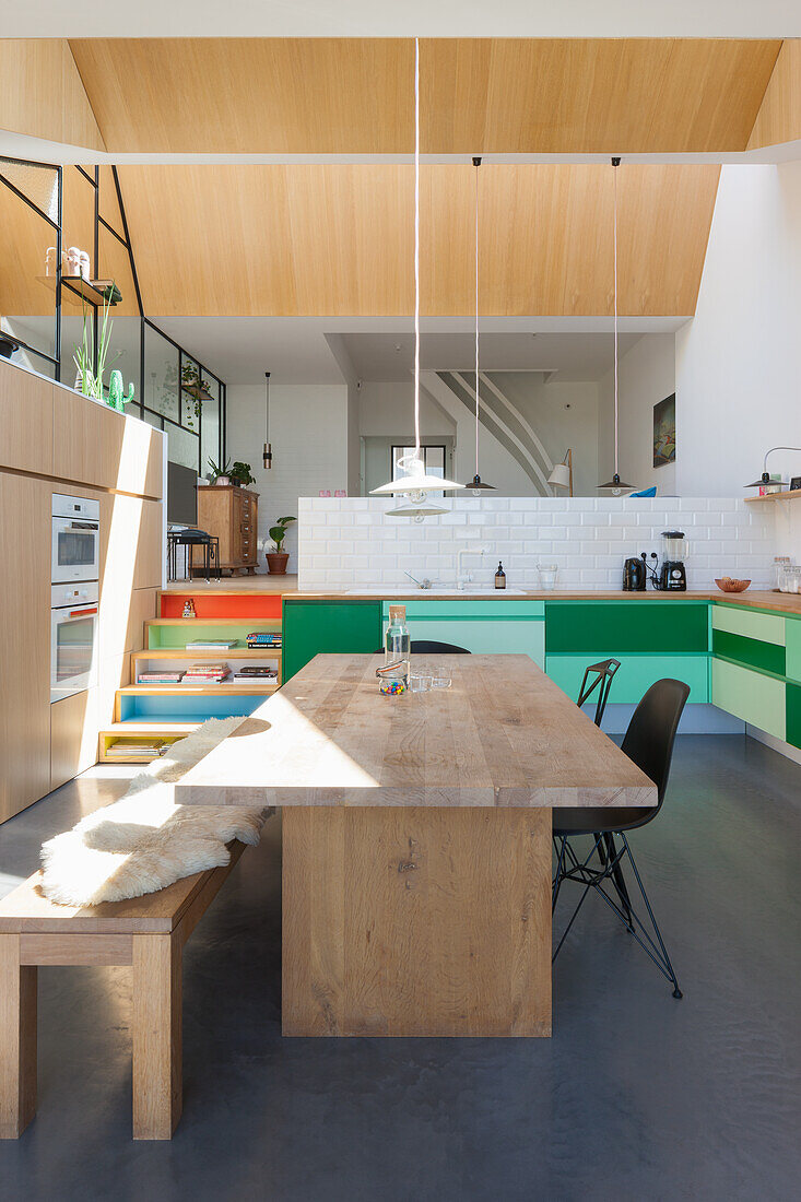 Open-plan kitchen with solid wood table, modern pendant lights and bright color accents
