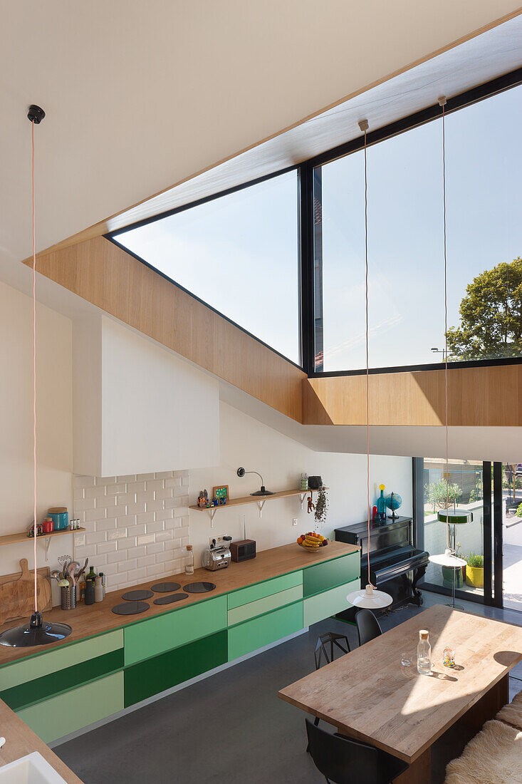 Modern, bright kitchen area with green base cabinets and large windows