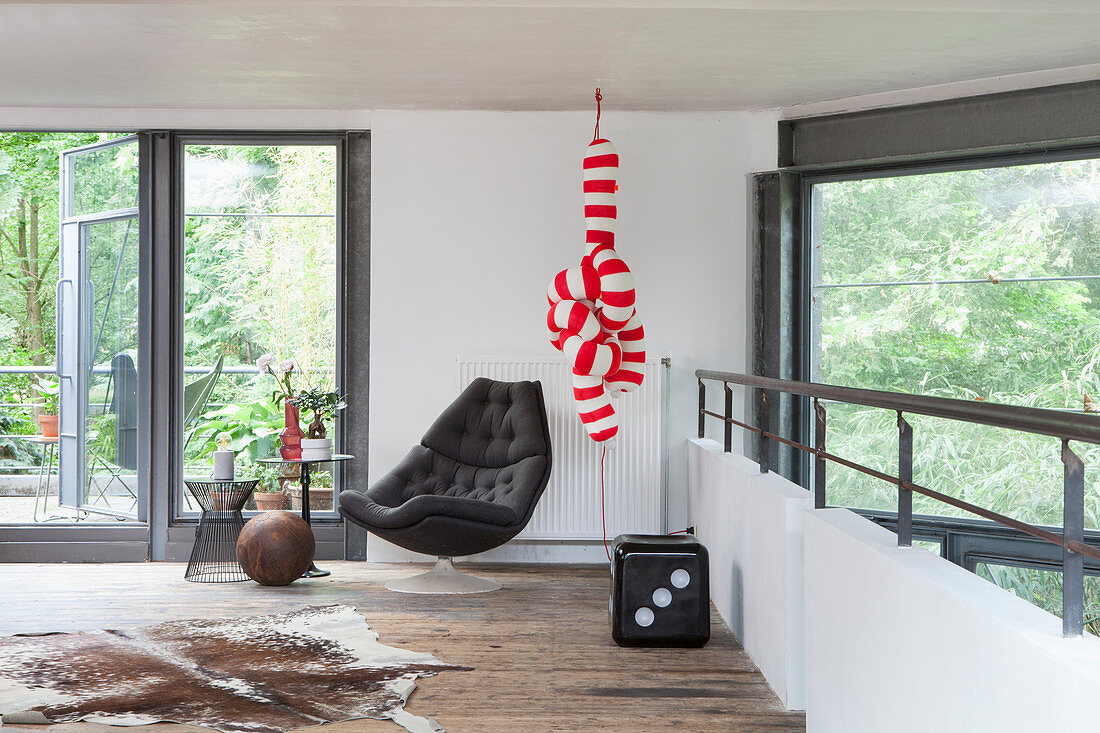 Schwarzer Sessel, Tierfellteppich, Sitzwürfel und rot-weiß gestreiftes Dekoobjekt