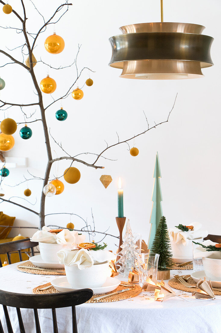 Branch decorated with yellow and petrol baubles on set table