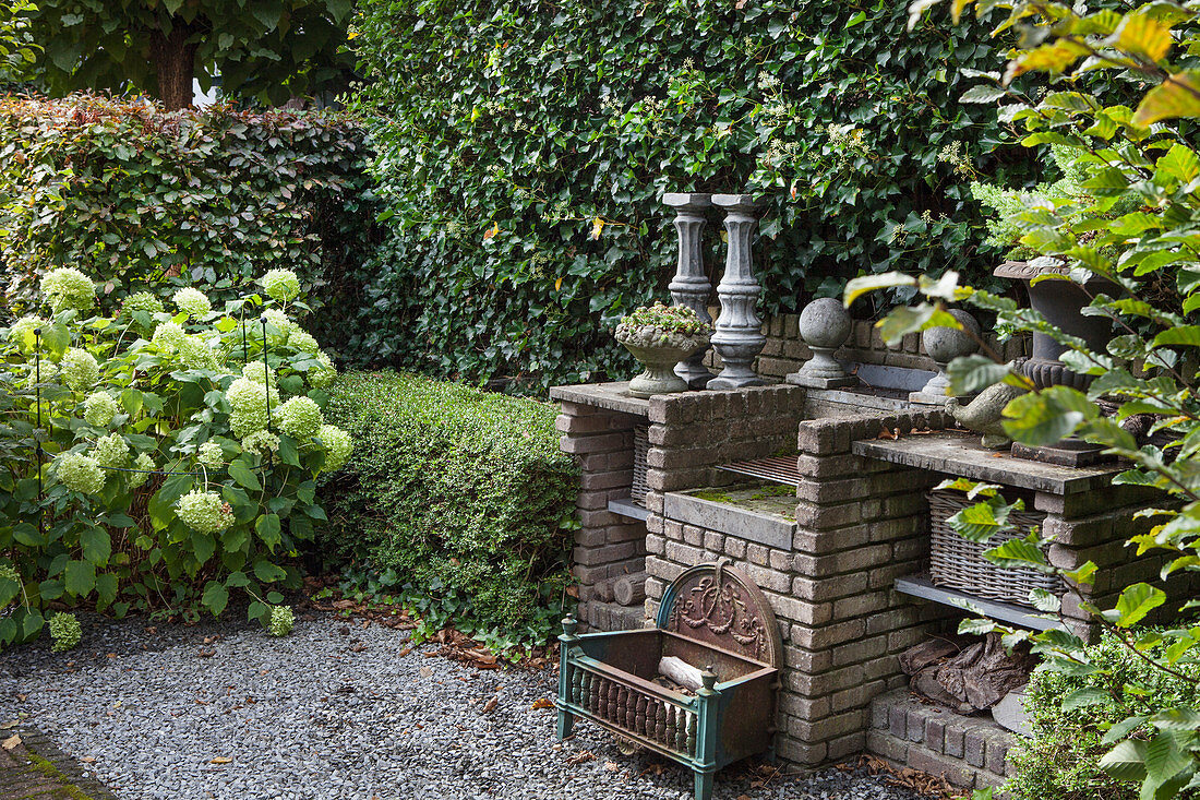 A brick outdoor kitchen in front of a hedge in an autumnal garden