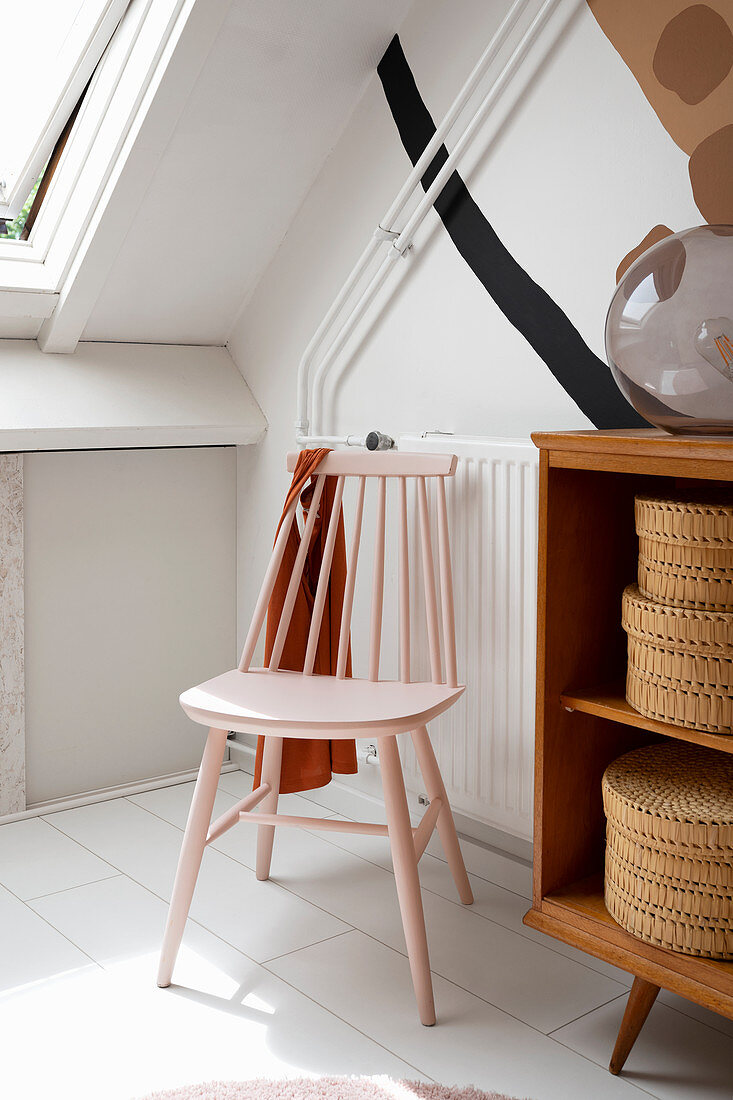 Pink spoke-back chair next to knee wall with fitted cupboards