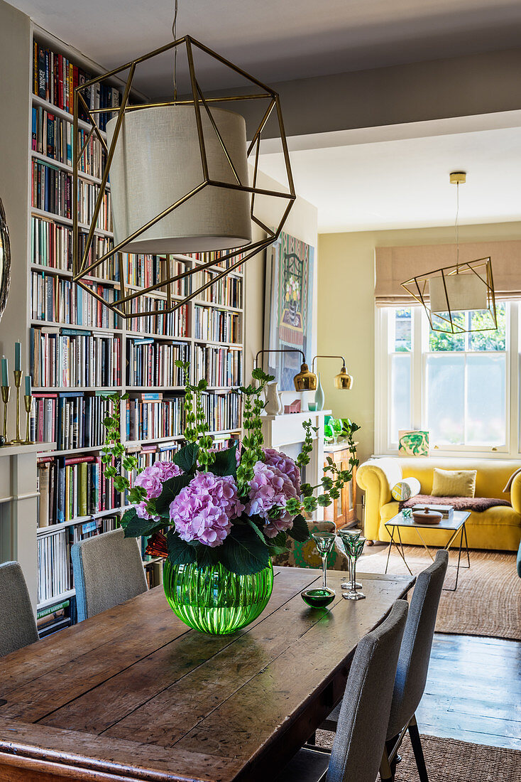 Holztisch mit Blumenstrauß vor raumhohem Bücherregal