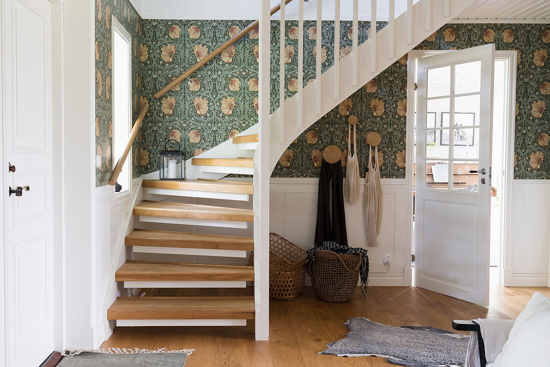 An entrance hall with wooden stairs, white cassette cladding and wallpaper