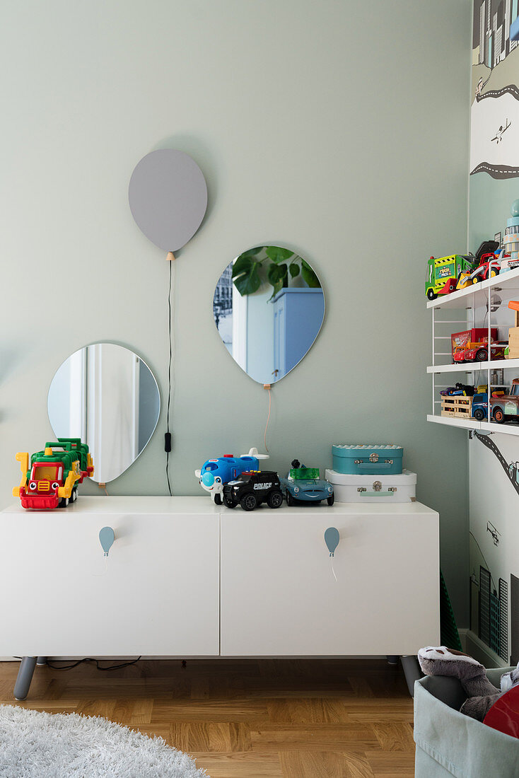 A lowboard in a children's room with a balloon lamp above it and a mirror on the wall