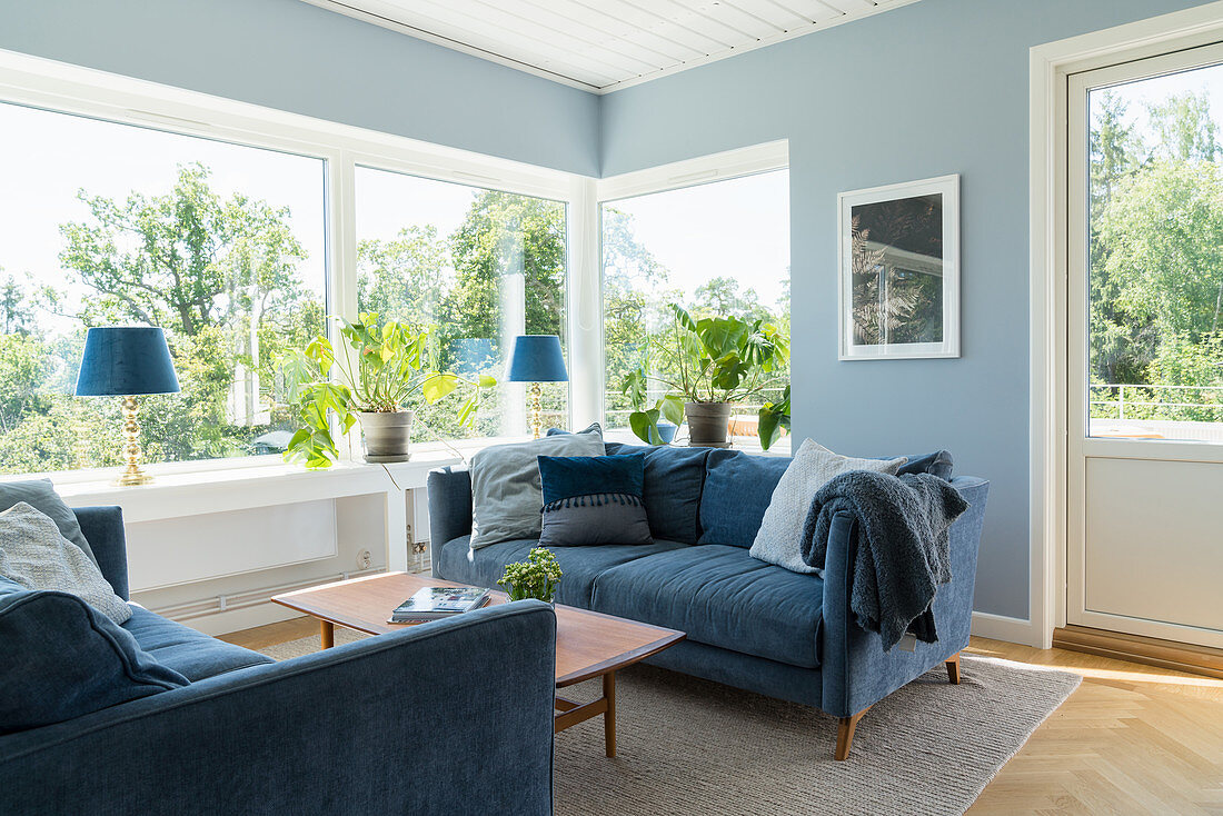 A blue sofa suite in a living room with a banks of windows