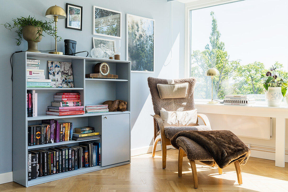 Gemütlicher Stuhl mit Fussschemel und Bücherregal vor Fenster im Wohnzimmer